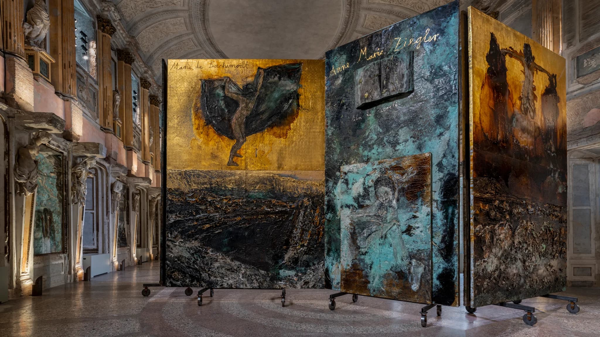 Installation view of Anselm Kiefer’s “The Women Alchemists” at Palazzo Reale, Sala delle Cariatidi, Milan, featuring monumental textured panels with alchemical and figurative imagery.