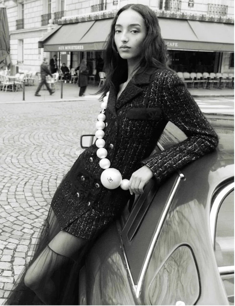 Black-and-white Paris street photo of a model in a tweed coat and sheer skirt.