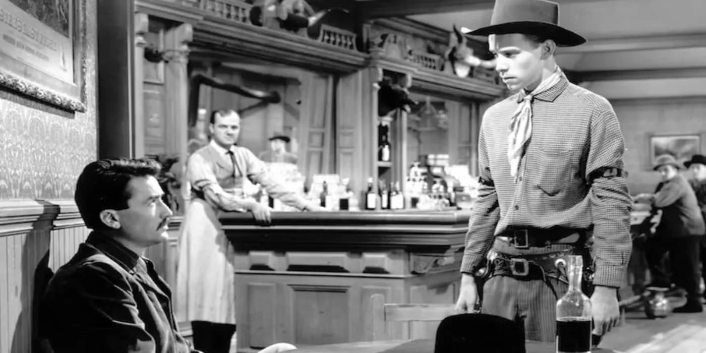 Gregory Peck as the gunfighter Jimmy Ringo sitting alone at a bar, seen from behind, in a dim saloon interior from the film The Gunfighter (1950).