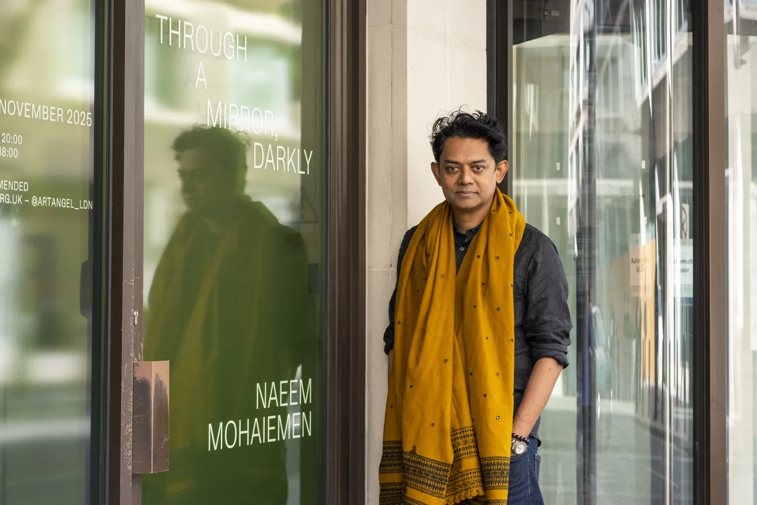 Artist Naeem Mohaiemen standing outside his Artangel exhibition Through a Mirror, Darkly in London, wearing a mustard shawl.