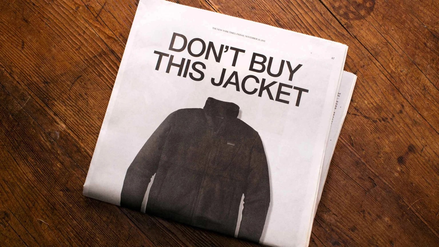 Newspaper laid on a wooden table with a large black-and-white advertisement showing a jacket and the bold headline DONT BUY THIS JACKET.