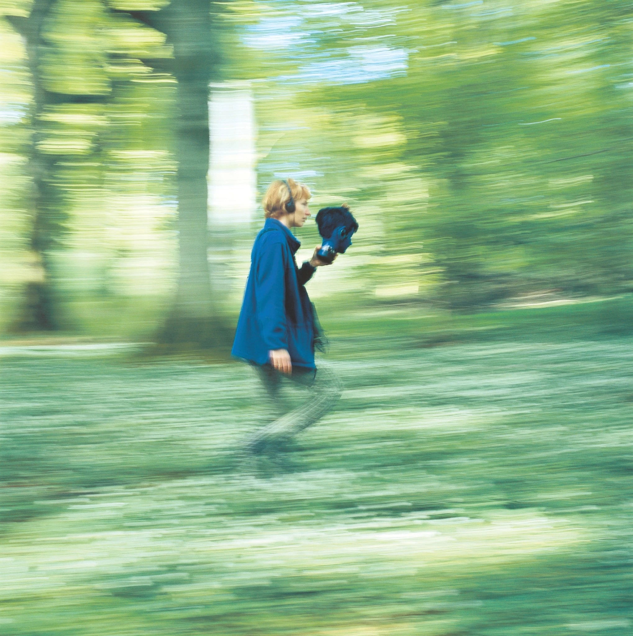 Motion-blurred photograph of a participant walking through a wooded landscape while holding a recording device, documenting Janet Cardiff’s site-specific audio walk Wans Walk.