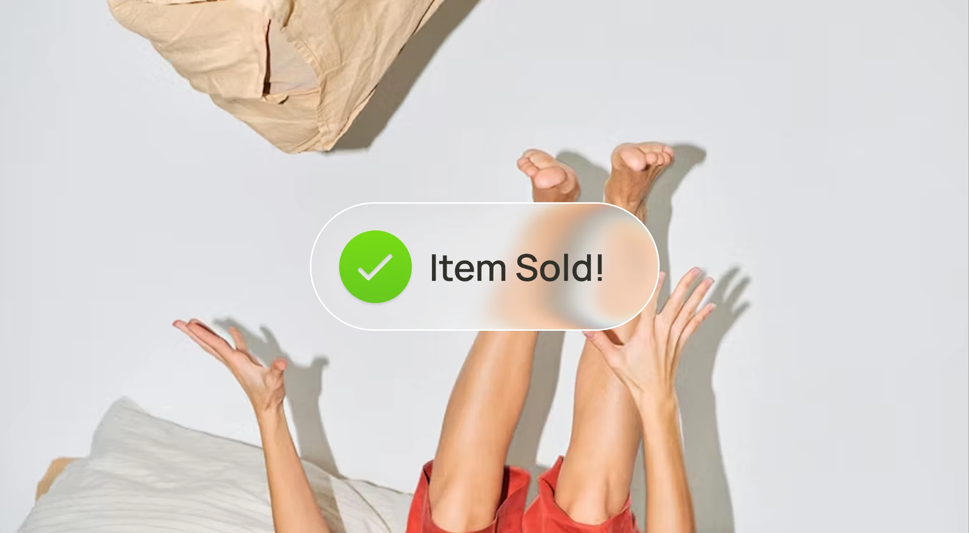 Minimal ecommerce style image showing a person lying on a bed with legs and arms raised in the air while a floating interface badge with a green checkmark reads “Item Sold!” over the scene.