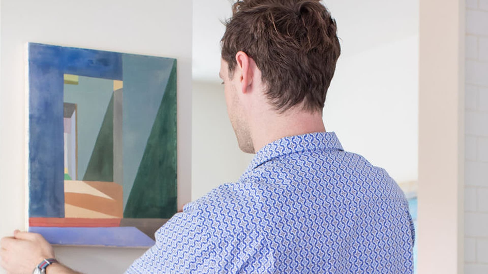 Craig Follett, CEO of Peggy, hanging abstract geometric painting on white gallery wall