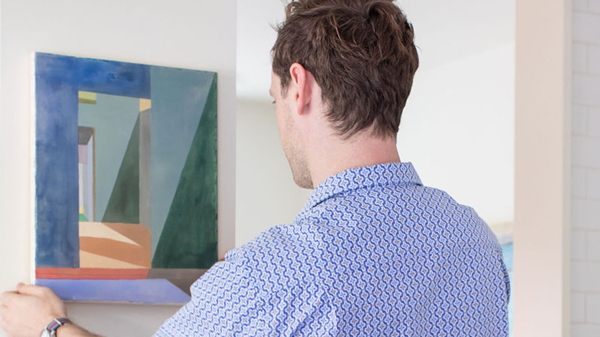 Craig Follett, CEO of Peggy, hanging abstract geometric painting on white gallery wall