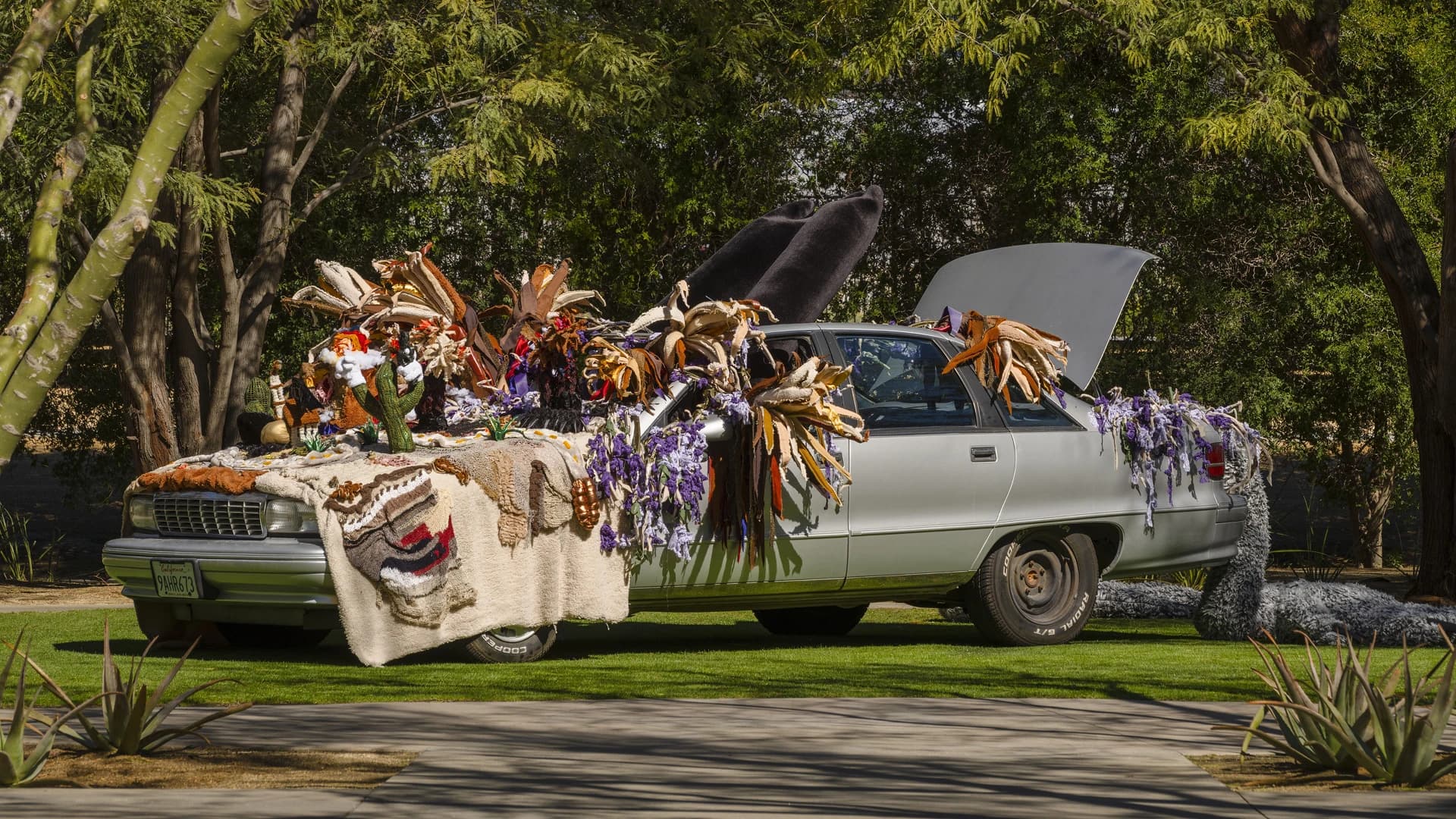 Paloma Contreras Lomas art installation: vintage white sedan adorned with feathers, purple garlands, and folk objects outdoors