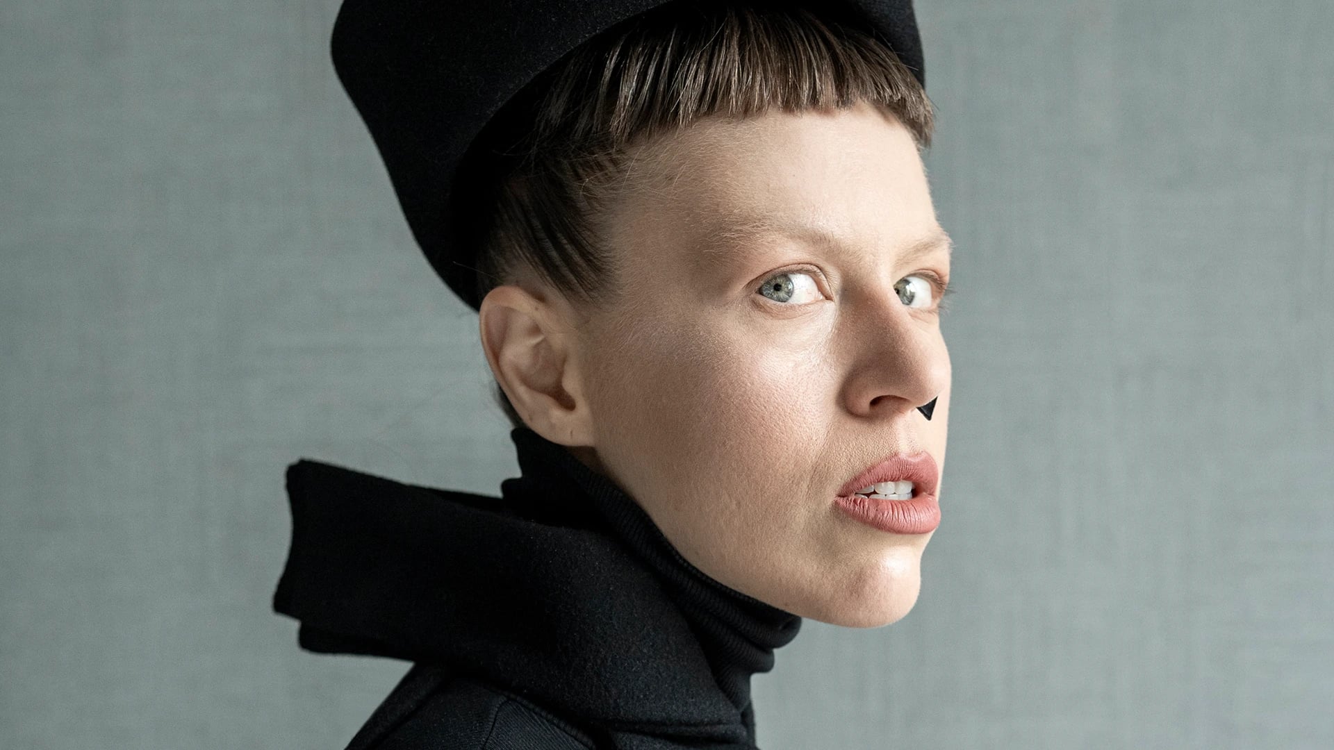 Irina Dzhus in sculptural black turtleneck and structured cap, portrait by Lukas Klimek