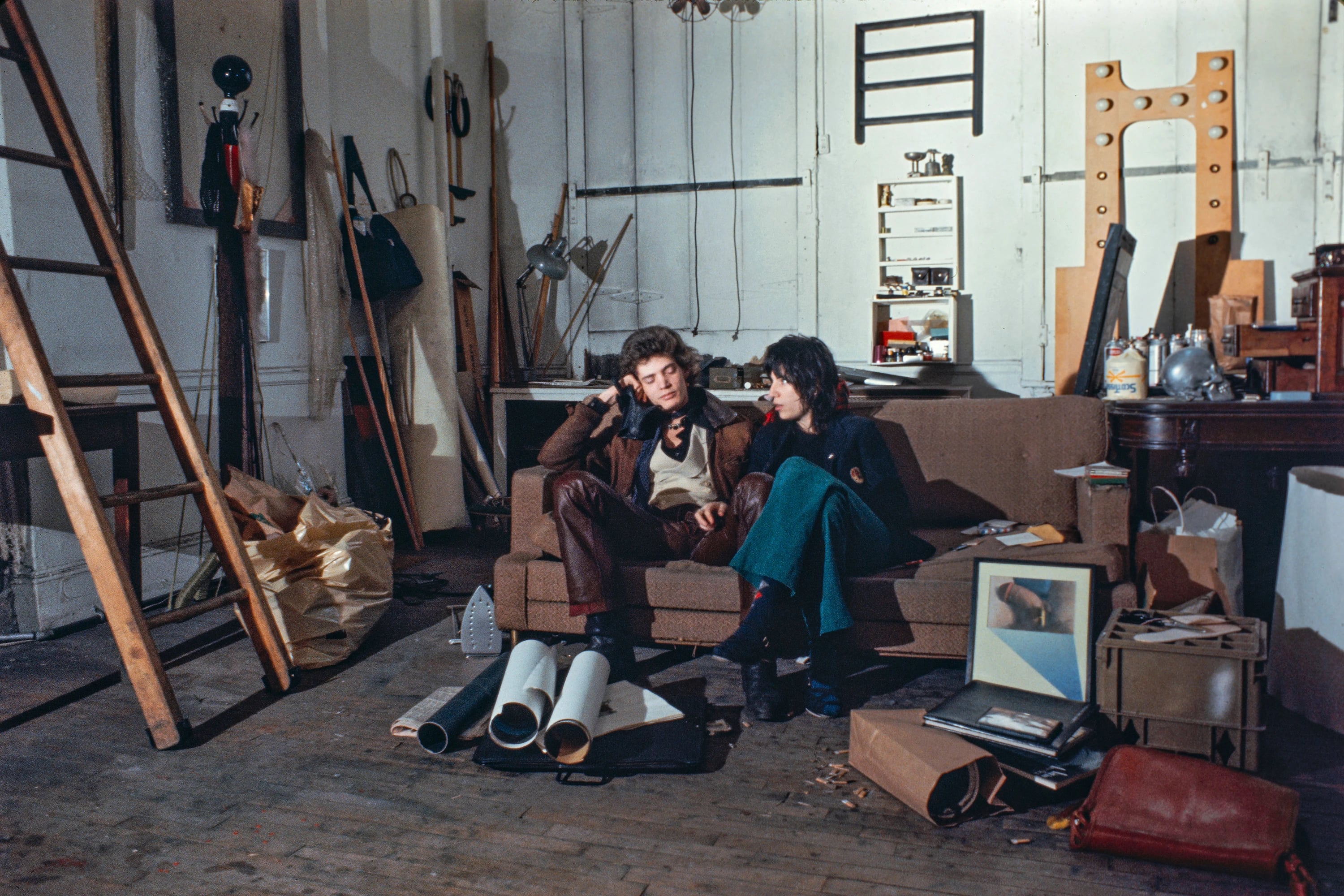Robert Mapplethorpe and Patti Smith seated in a cluttered Chelsea Hotel studio, 1970, photographed by Albert Scopin