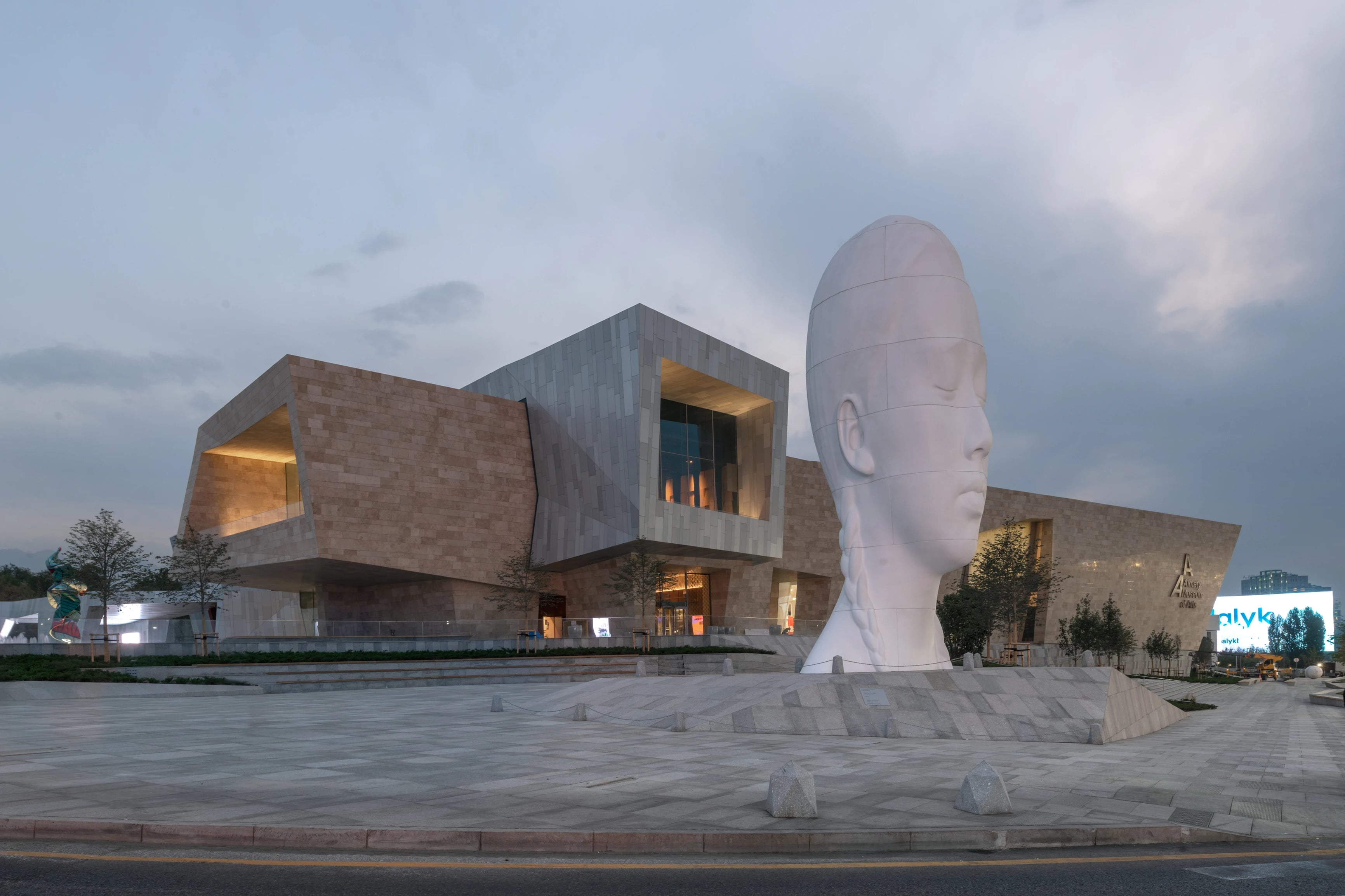 Monumental white sculptural face with closed eyes outside the Almaty Museum of Arts at dusk