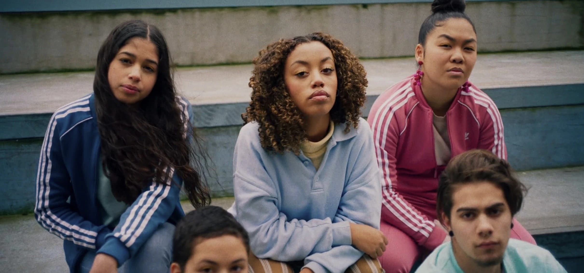 A group of five individuals in activewear sit on concrete stairs, with disdained expressions on their faces. Mikki Sindhunata