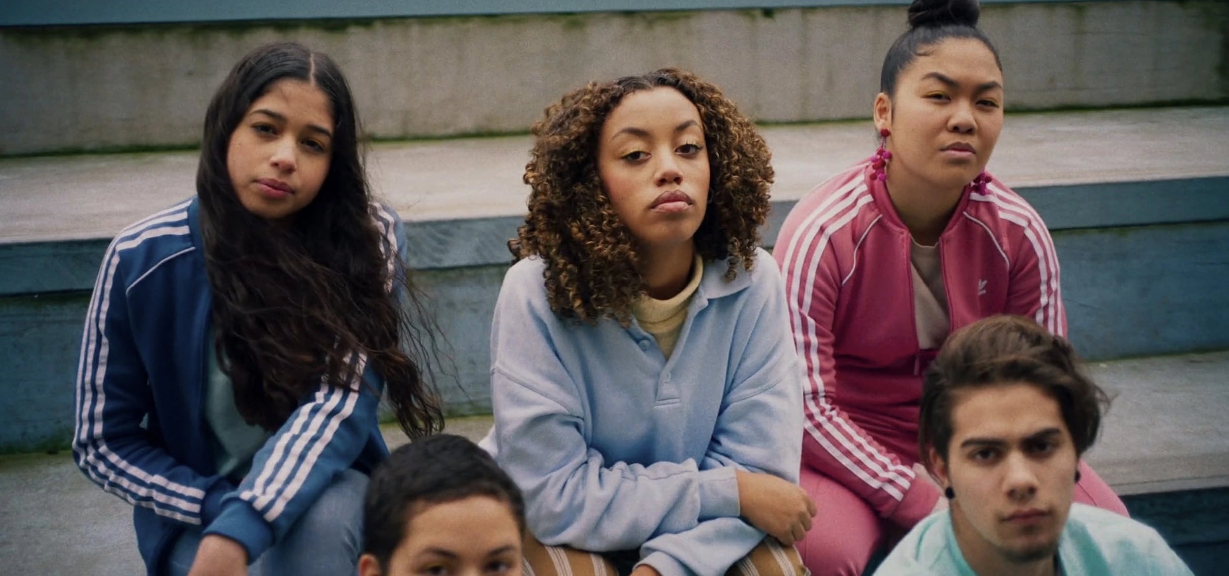 A group of five individuals in activewear sit on concrete stairs, with disdained expressions on their faces. Mikki Sindhunata