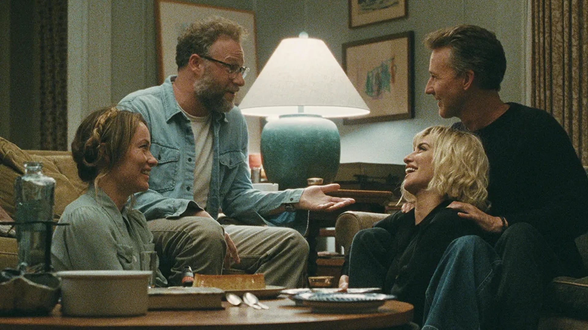 Four friends laughing together on a couch in a warmly lit living room, from The Invite (2026) directed by Olivia Wilde